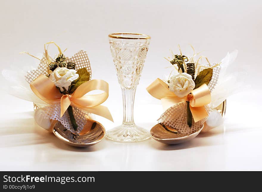 A small glass standing between 2 decorated spoons. A small glass standing between 2 decorated spoons