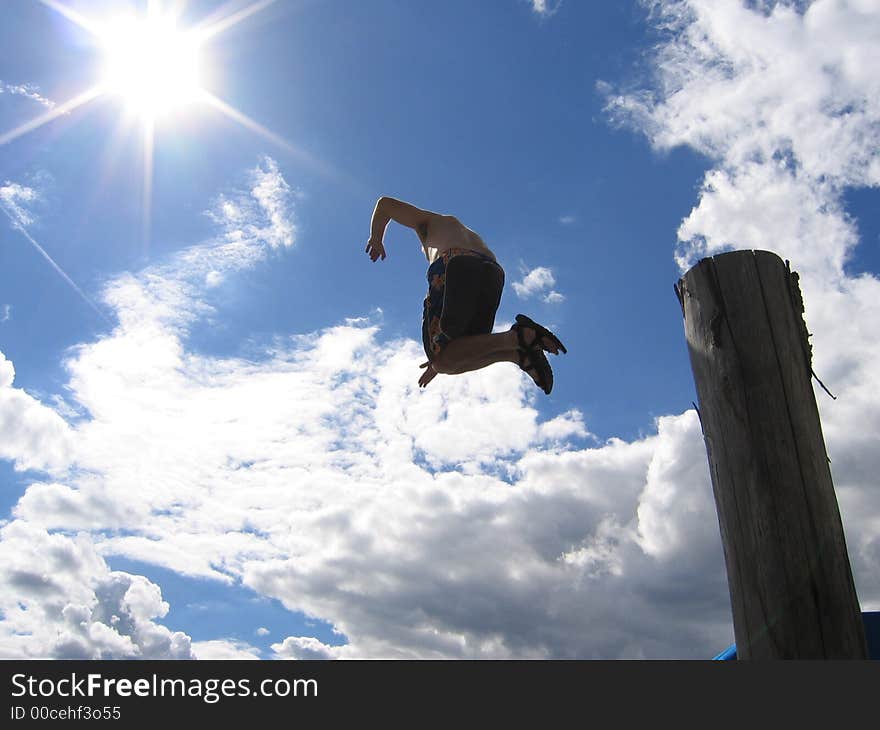 Man jumps off piling under sun and blue sky. Man jumps off piling under sun and blue sky.