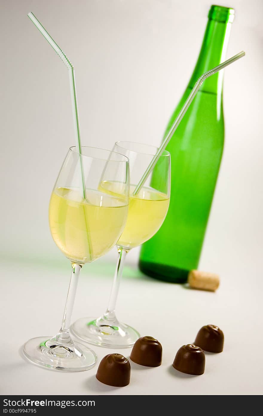 Green bottle, two glasses with yelllow liquid and straws, four chocolates. Green bottle, two glasses with yelllow liquid and straws, four chocolates.