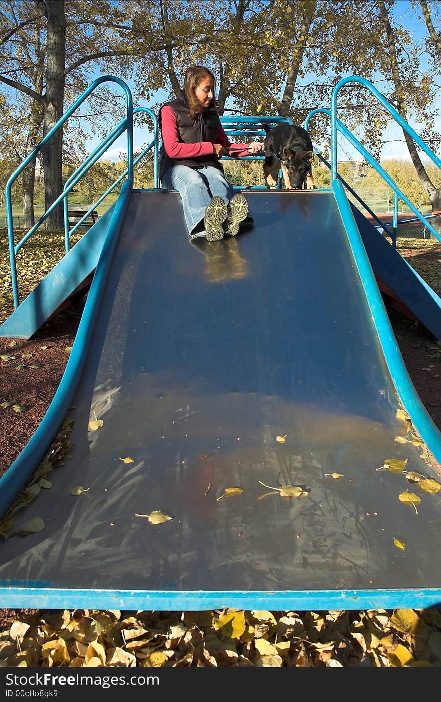 Young woman and her German Shepherd puppy ready to ride on a slide at the playground. Young woman and her German Shepherd puppy ready to ride on a slide at the playground.