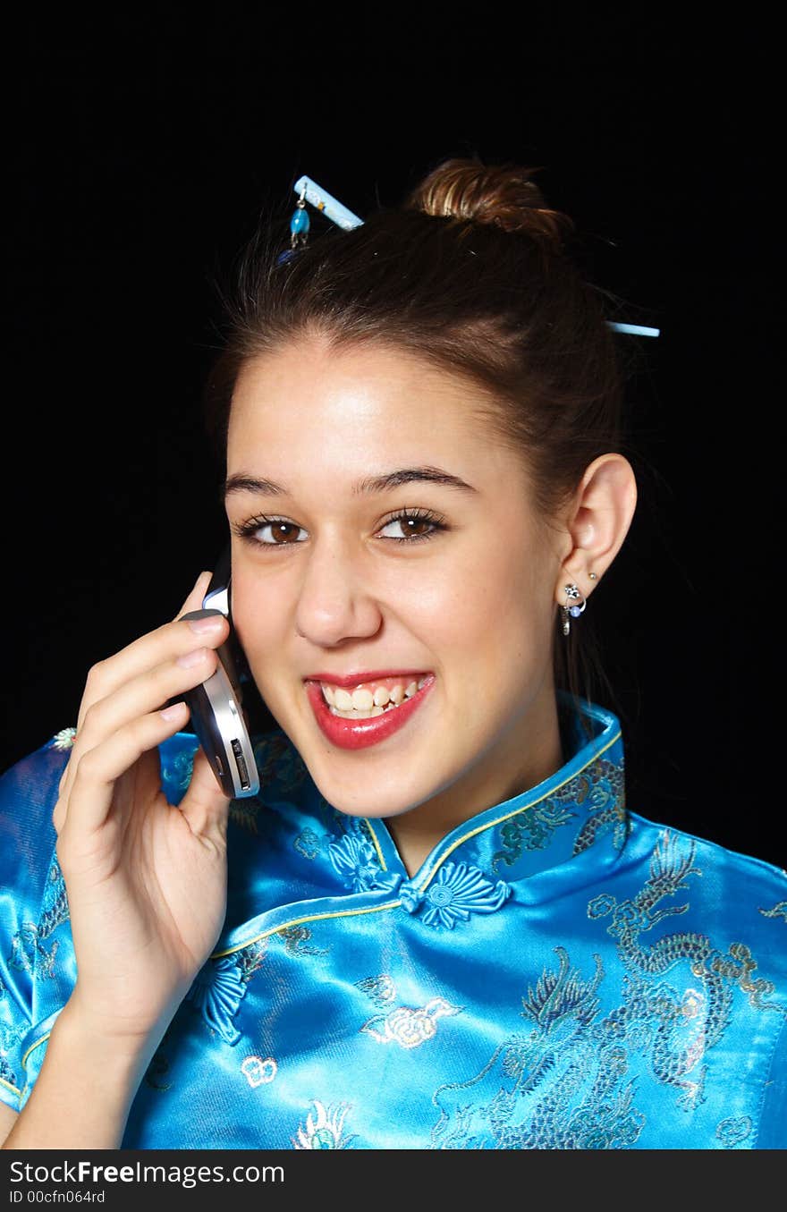 A young woman, in oriental dress smiles as she talks on her cell phone. A young woman, in oriental dress smiles as she talks on her cell phone.