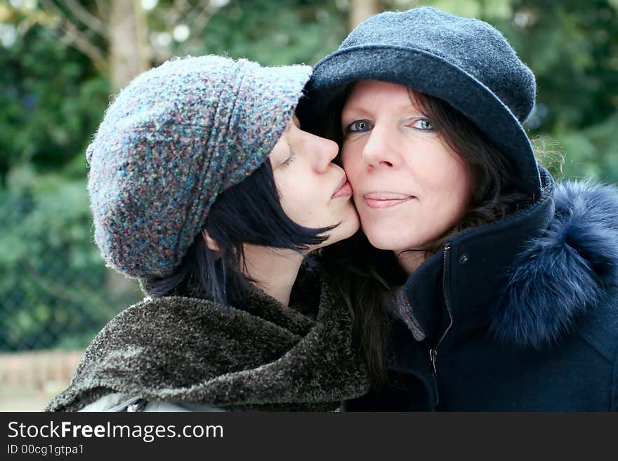 Mother and daughter, outdoor, warm clothes ,  closed together, close-up, giving a kiss. Mother and daughter, outdoor, warm clothes ,  closed together, close-up, giving a kiss