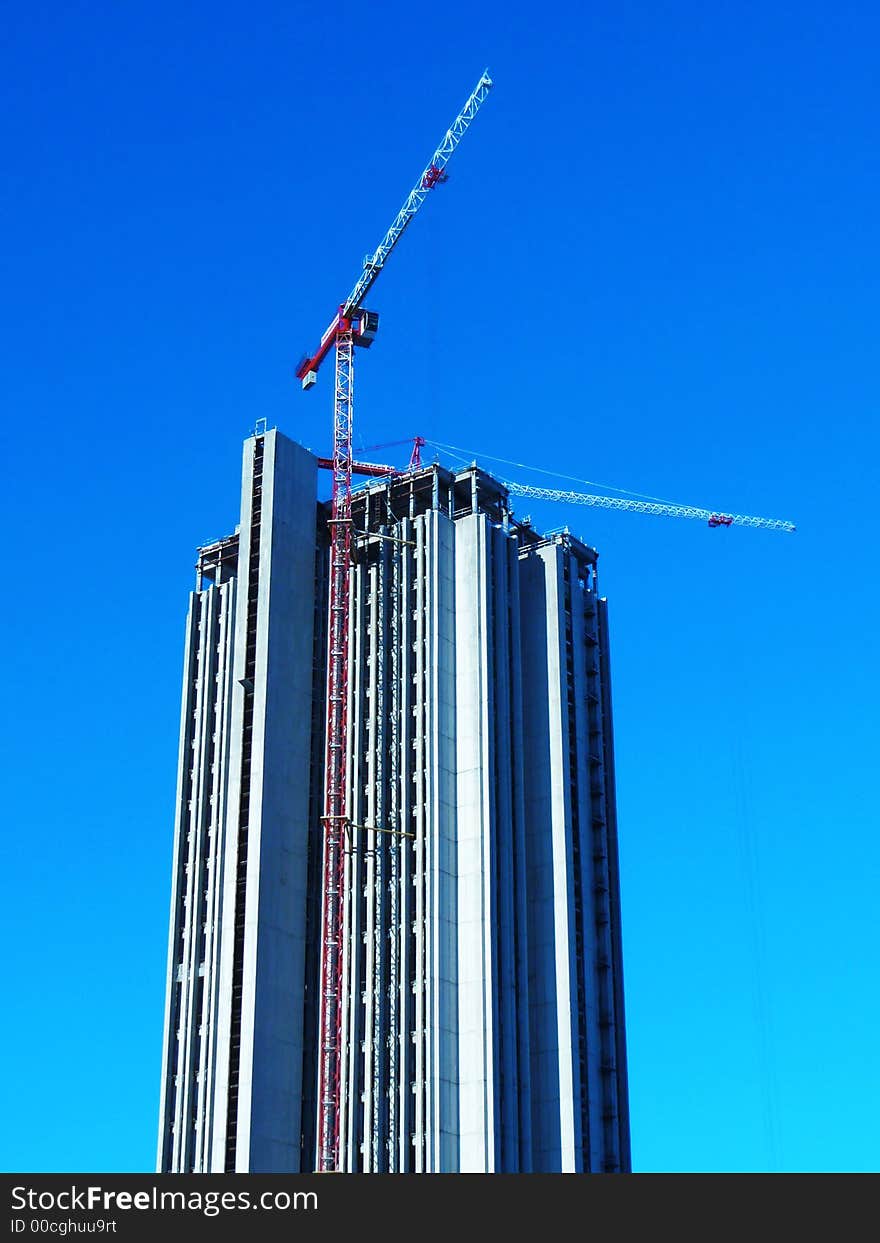 Two hoisting cranes building skyscraper office block in bright blue sky. Two hoisting cranes building skyscraper office block in bright blue sky