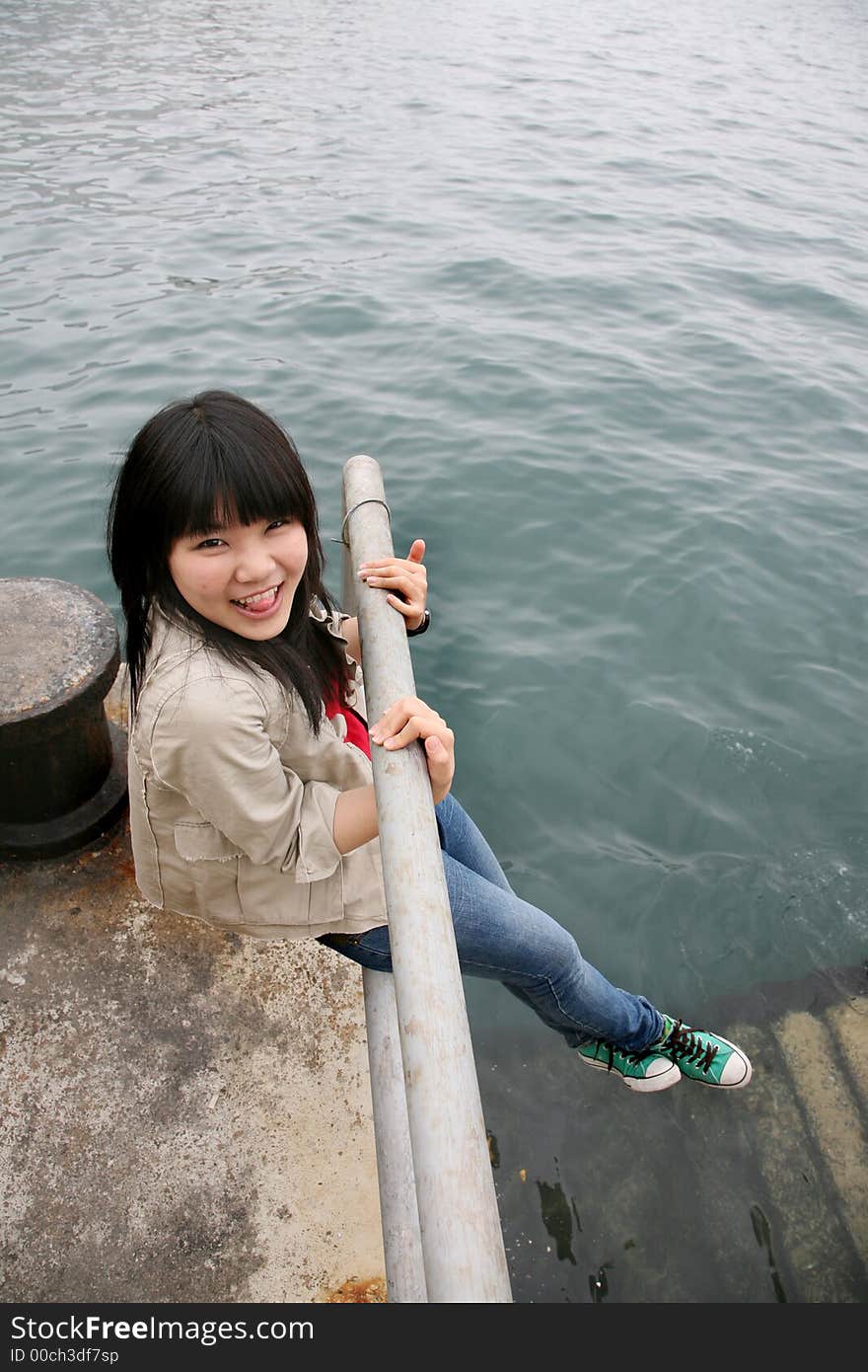 Asian girl smiling holding onto railing with legs hanging. Asian girl smiling holding onto railing with legs hanging