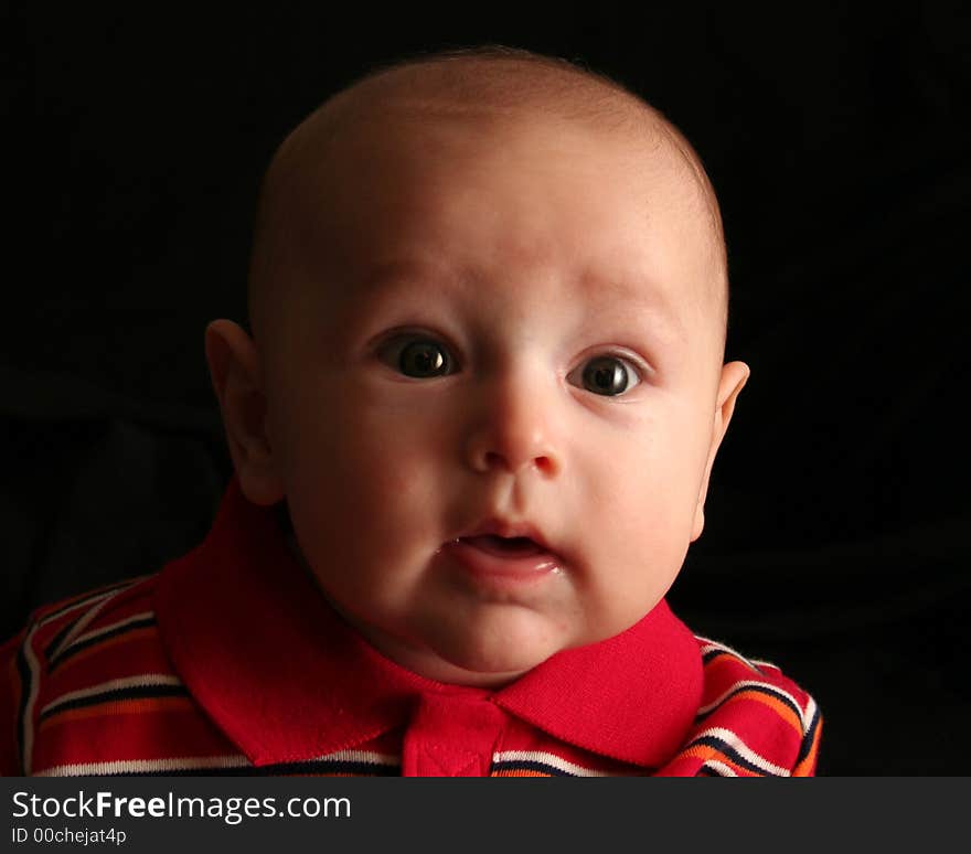 The face of a baby boy posing for the camera on a black background. The face of a baby boy posing for the camera on a black background.