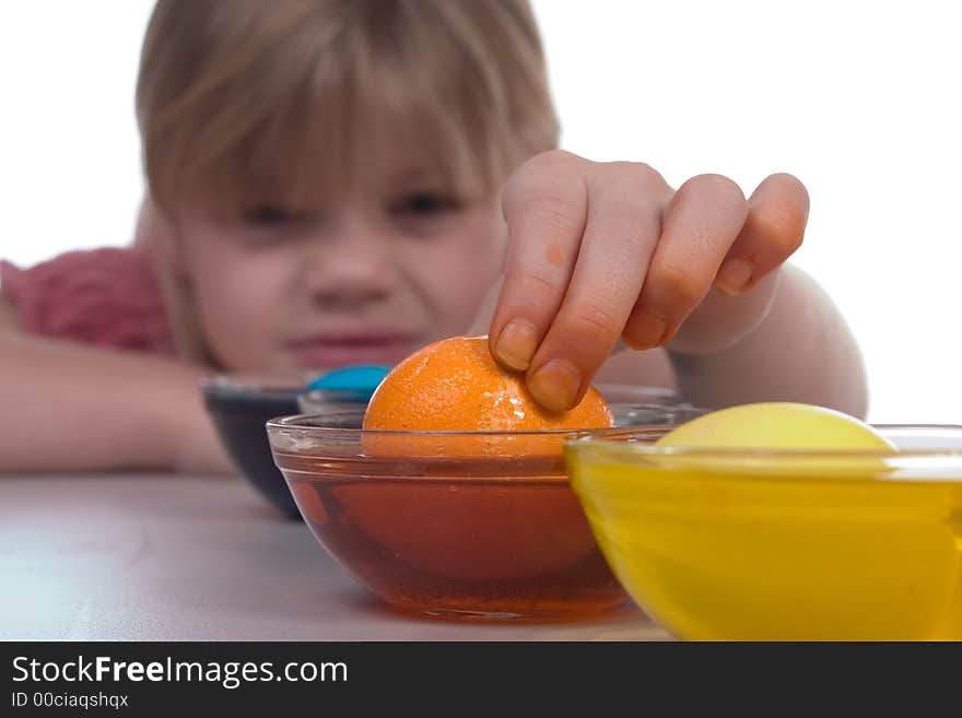 Young girl coloring easter eggs. Image has shallow focus; emphasizing the orange egg being picked up from the dye.