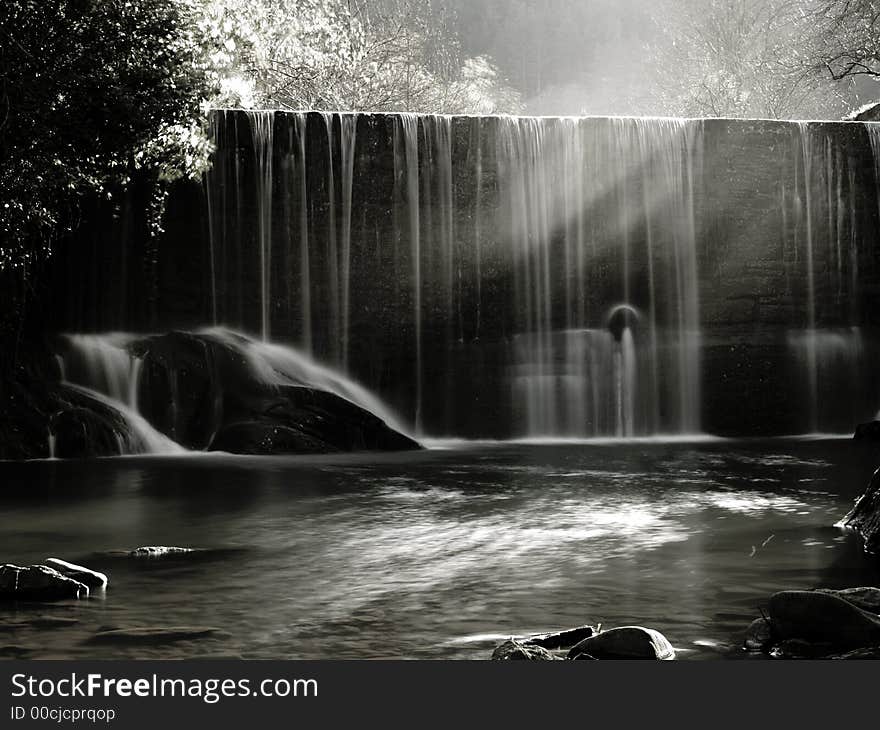 A scenic waterfall stream in silky effect, sun light beams from coming from the left. A scenic waterfall stream in silky effect, sun light beams from coming from the left