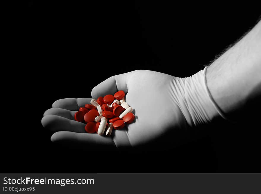 Hand with medical glove holding pills over black background