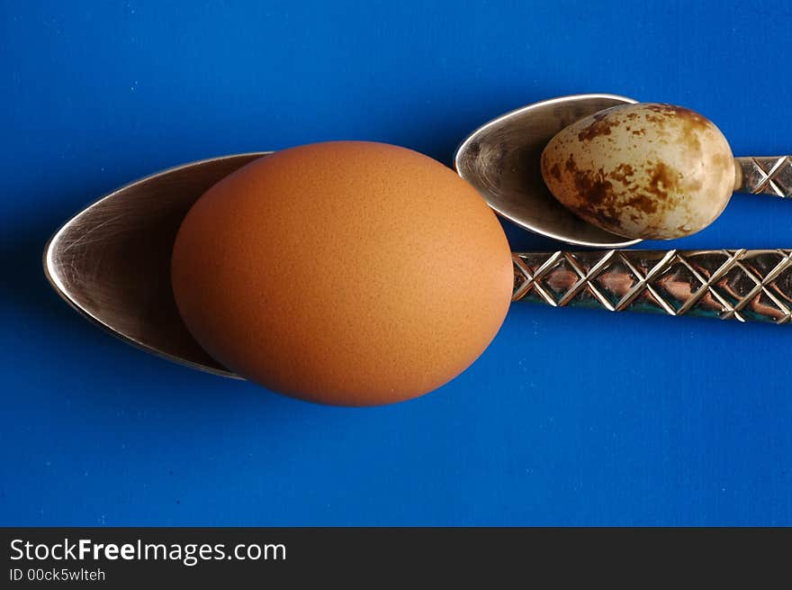 Two eggs and two spoons on blue background. Two eggs and two spoons on blue background