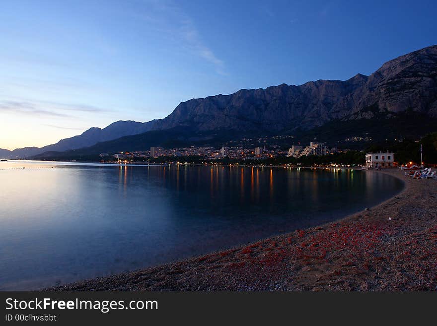 Small houses in the distance, dusk light, water with no objects, interesting texture of the shore. Small houses in the distance, dusk light, water with no objects, interesting texture of the shore.