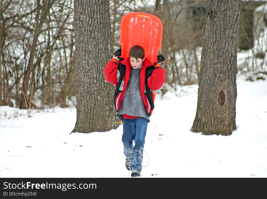 A Boy carrying his sled on his back. A Boy carrying his sled on his back