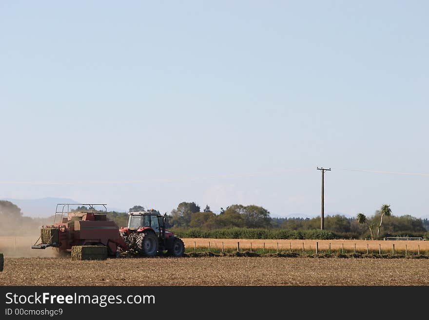 Tractor working to bale pea straw on the Canterbury Plains, New Zealand. Tractor working to bale pea straw on the Canterbury Plains, New Zealand