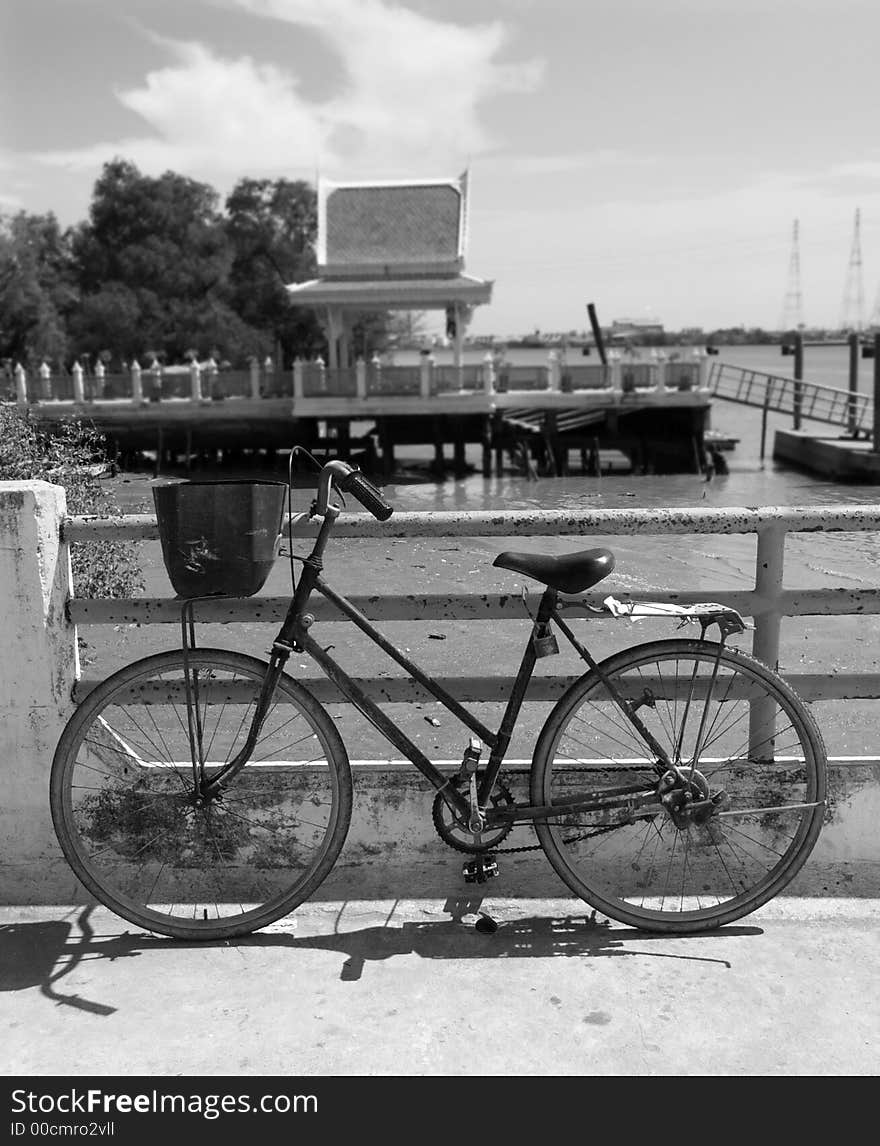 Old bicycle waiting at a quay along the Chao Praya river in Samut Prakan, Thailand. Black and white photo with background out of focus. Old bicycle waiting at a quay along the Chao Praya river in Samut Prakan, Thailand. Black and white photo with background out of focus.