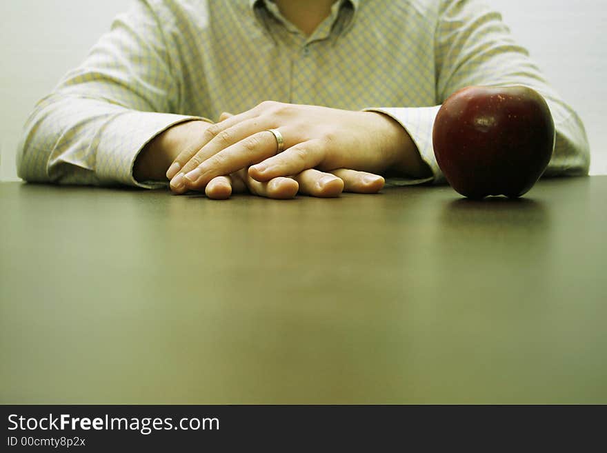 Male hands on a brown table and an apple. Male hands on a brown table and an apple