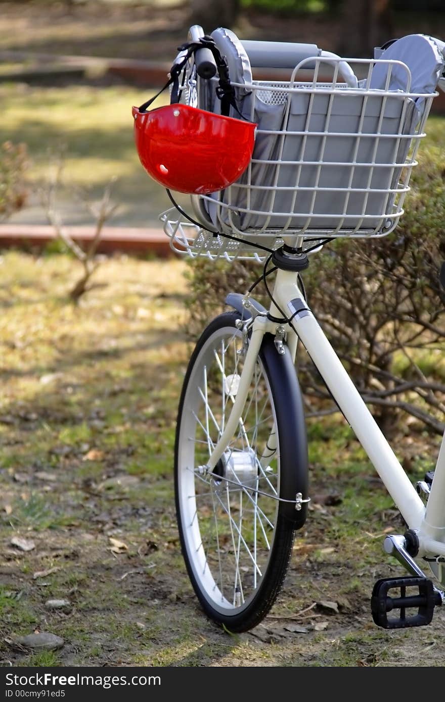 Image of a bicycle handlebar with a kid helmet hanging down in a park. Image of a bicycle handlebar with a kid helmet hanging down in a park.