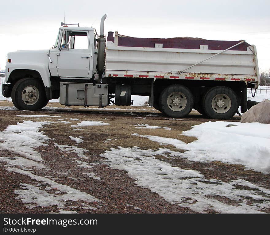 A side view of a white gravel truck parked outside after a delivery trip.