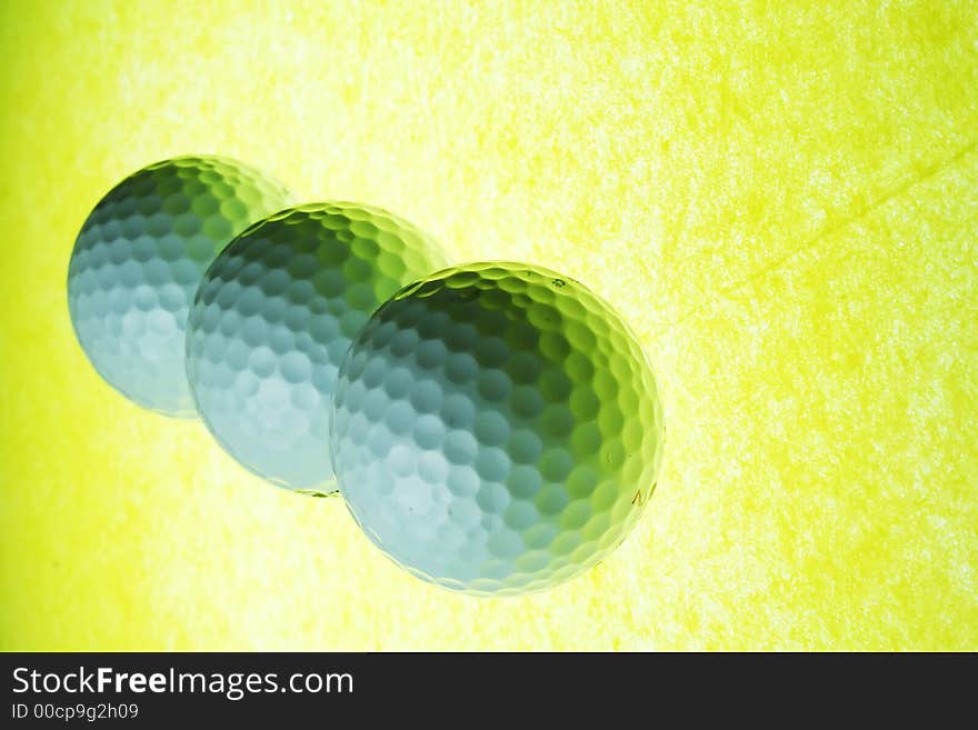 A trio of golf balls on yellow illuminated glass. A trio of golf balls on yellow illuminated glass