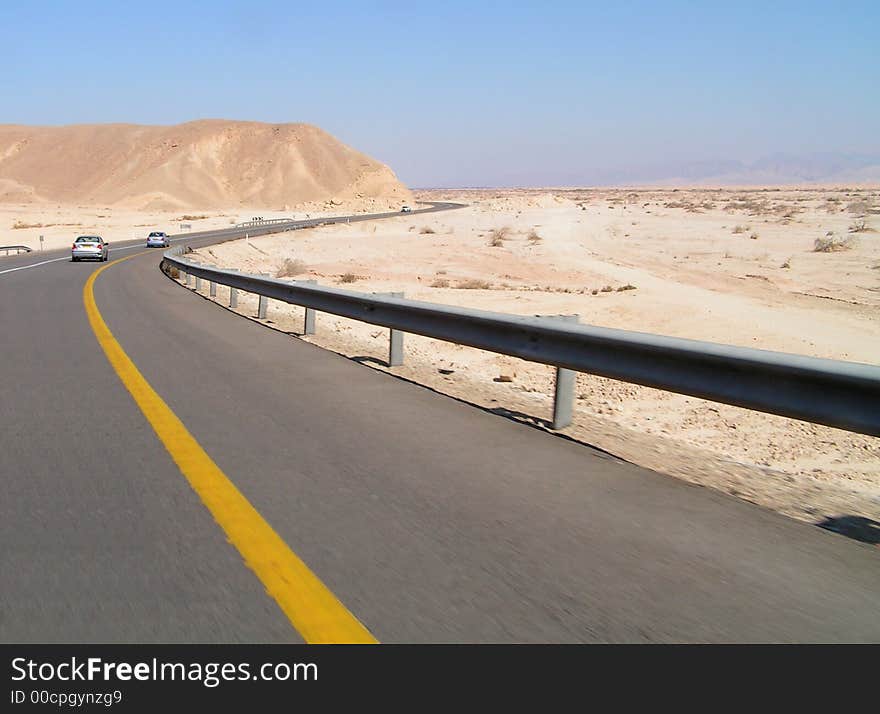 Asphalt road with two cars in Negev desert. Blue sky and desert around. Asphalt road with two cars in Negev desert. Blue sky and desert around