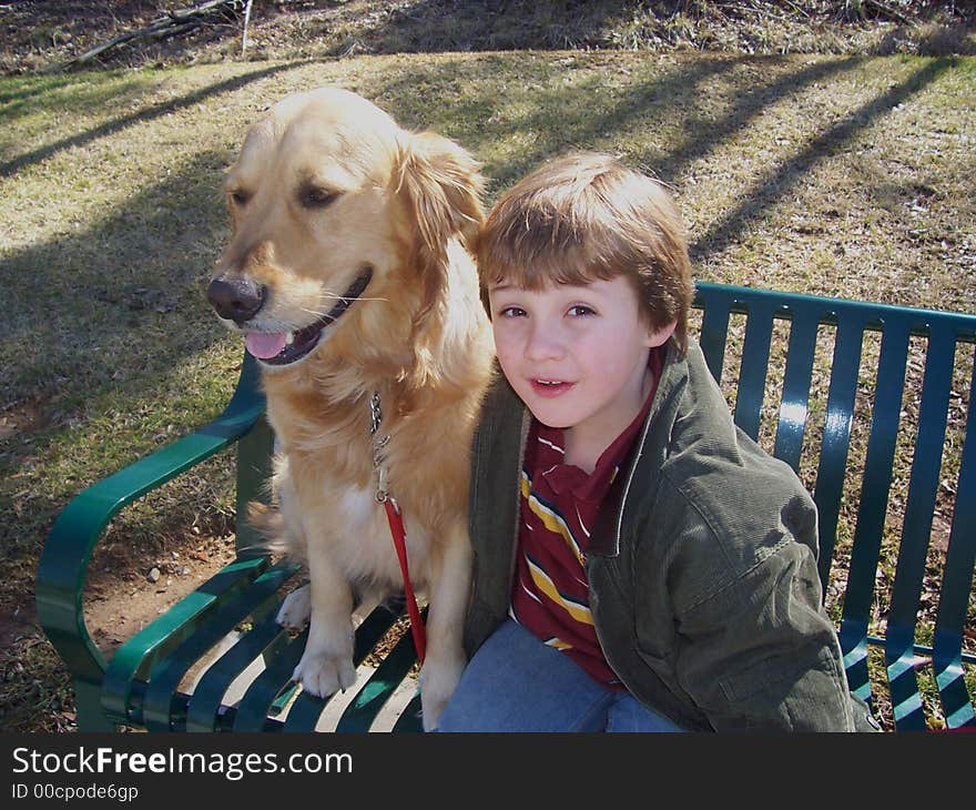 Young boy and golden retriever sitting on green bench in park. Young boy and golden retriever sitting on green bench in park