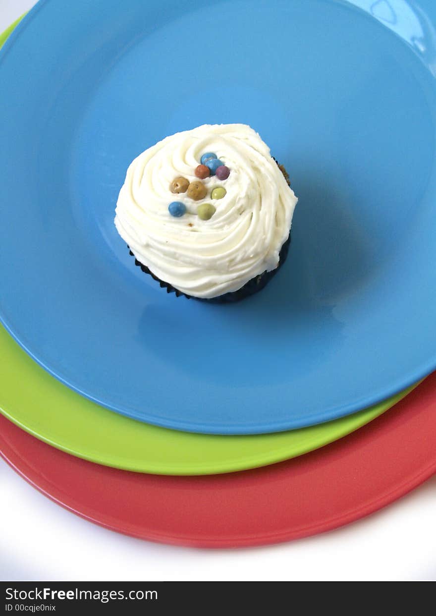 Three Ices cucpcake on a blue plate with coloured plates underneath. Three Ices cucpcake on a blue plate with coloured plates underneath