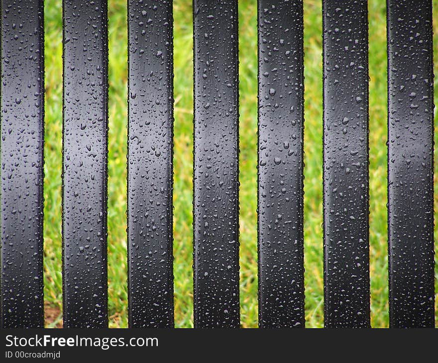 Black bench slats with rain drops, grass in background. Black bench slats with rain drops, grass in background