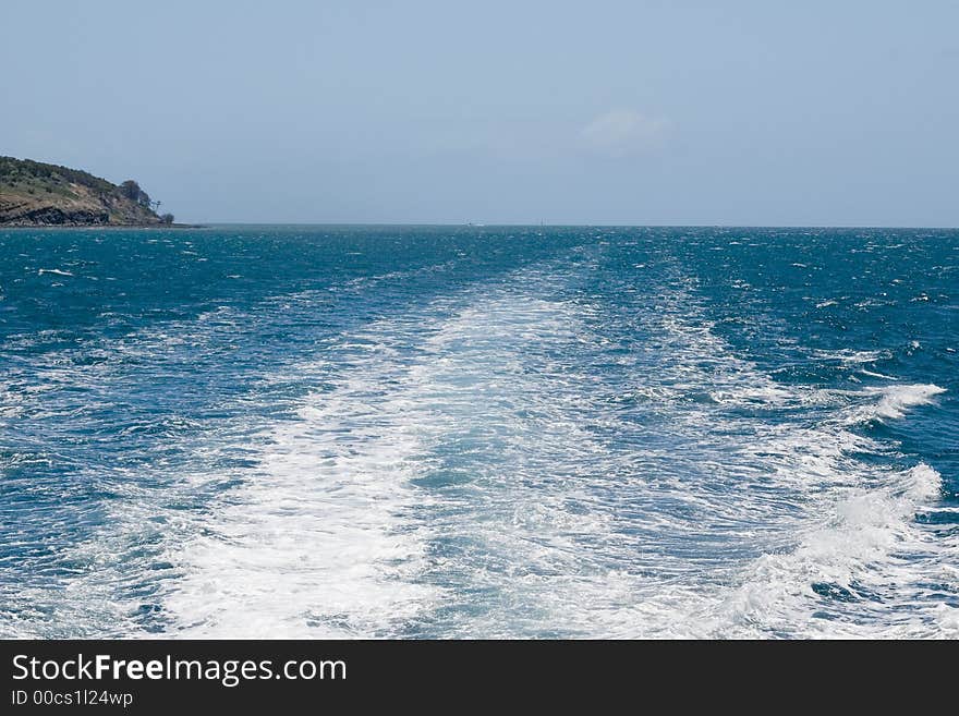 Looking out the back at a catamarans wake as it travels past an island. Looking out the back at a catamarans wake as it travels past an island