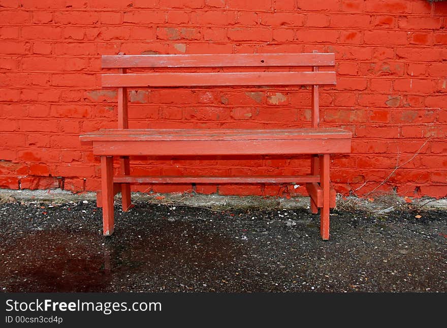 Old red bench by a red cracked brick wall. Old red bench by a red cracked brick wall