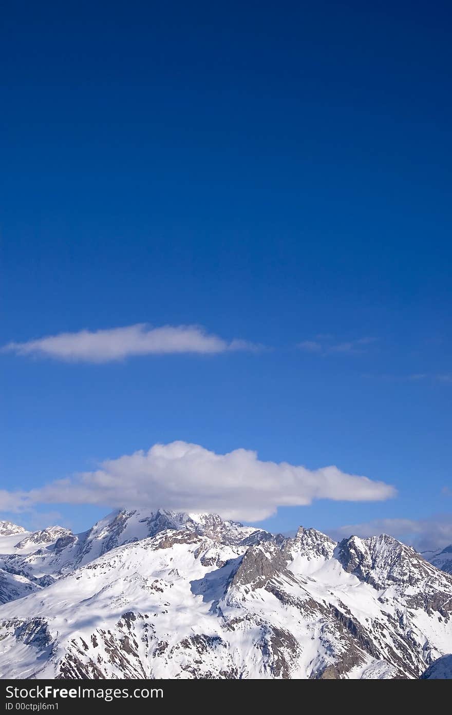 Snowed peak of a mountain surrounded by small cloud, a lot of blue for copy-space. Snowed peak of a mountain surrounded by small cloud, a lot of blue for copy-space