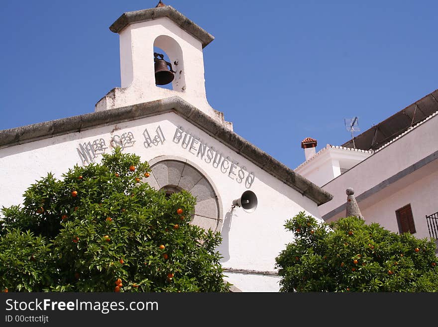 Orange trees are in front of white stone church en Castuera, Extremadura, Spain.