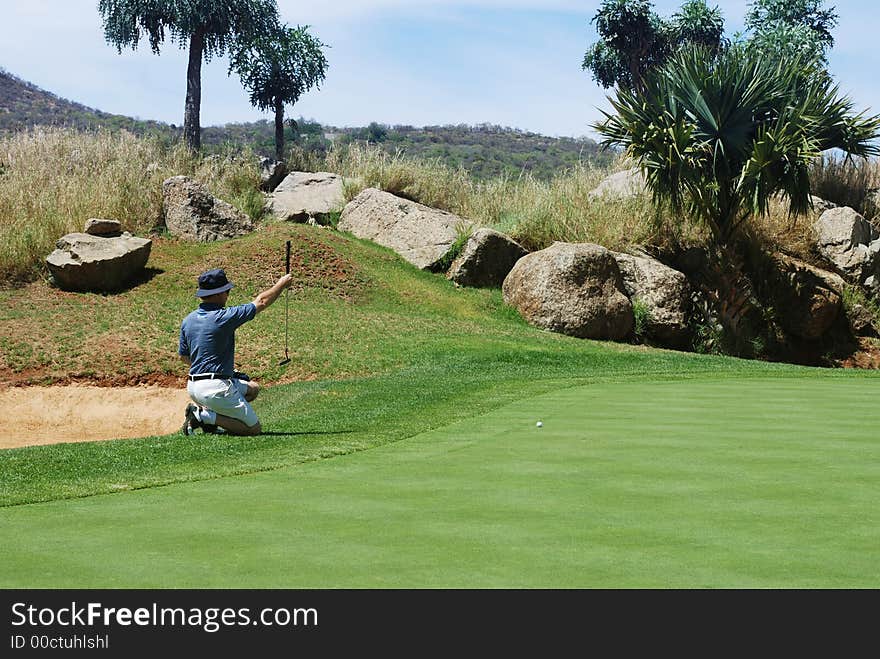 Middle age golfer sitting down next to the green, estimating the line for the putt. Middle age golfer sitting down next to the green, estimating the line for the putt.