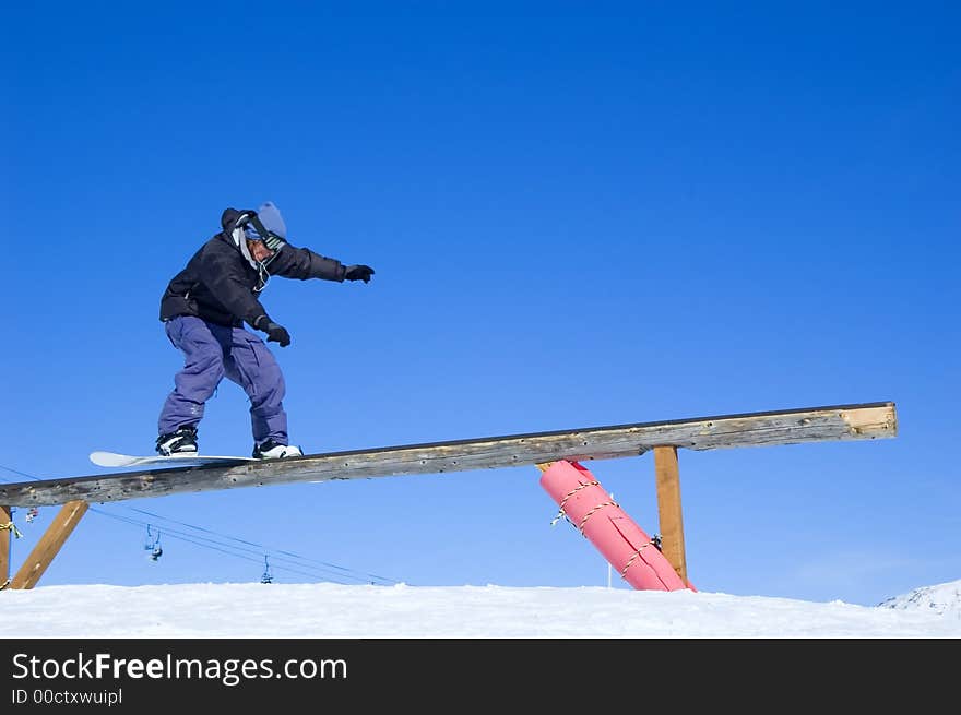 A snowboarder boardsliding on a wooden rail. A snowboarder boardsliding on a wooden rail