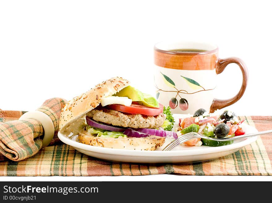 Turkey burger on an onion roll garnished with red onion, lettuce, egg avocado,and tomato slices served with a side of greek salad and a beverage. Turkey burger on an onion roll garnished with red onion, lettuce, egg avocado,and tomato slices served with a side of greek salad and a beverage.