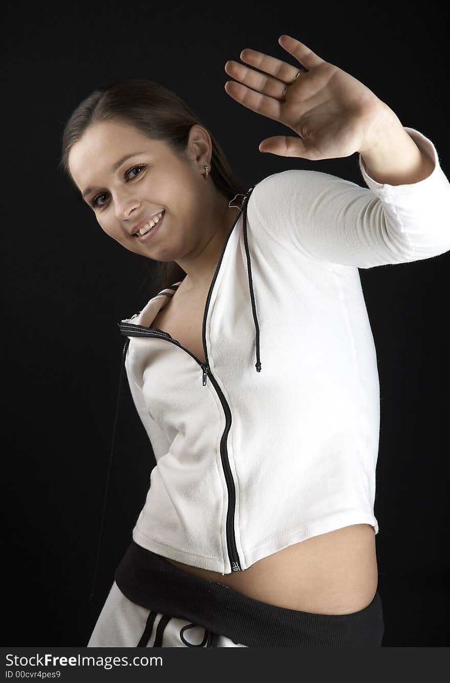 Smiling girl with raised hand in white sportive wear on black background. Smiling girl with raised hand in white sportive wear on black background