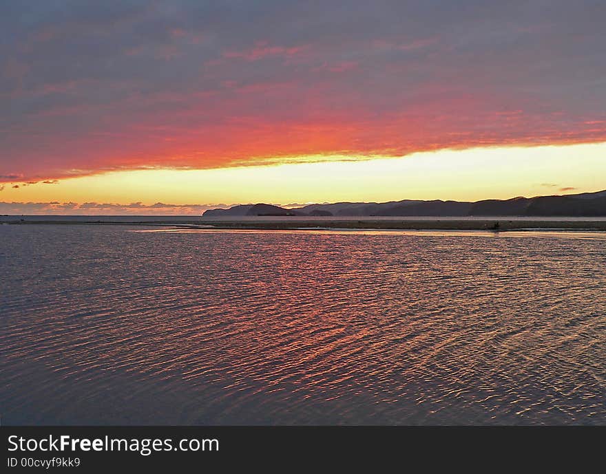 Sunset on seal. Dark clouds. The red and yellow highlights on water are on foreground. Islands and capes are on background. Russian Far East, Primorye, Japanese sea, Sokolovskaya bay, Petrova and Belcova islands.