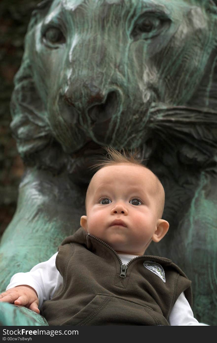 Image of cute baby sitting in front of a lion sculpture. Image of cute baby sitting in front of a lion sculpture