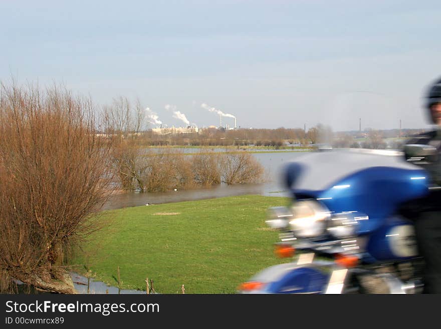 A motorcyclist and smoking factory-chimneys in a dutch riverscape. The forelands are swamped. A motorcyclist and smoking factory-chimneys in a dutch riverscape. The forelands are swamped.