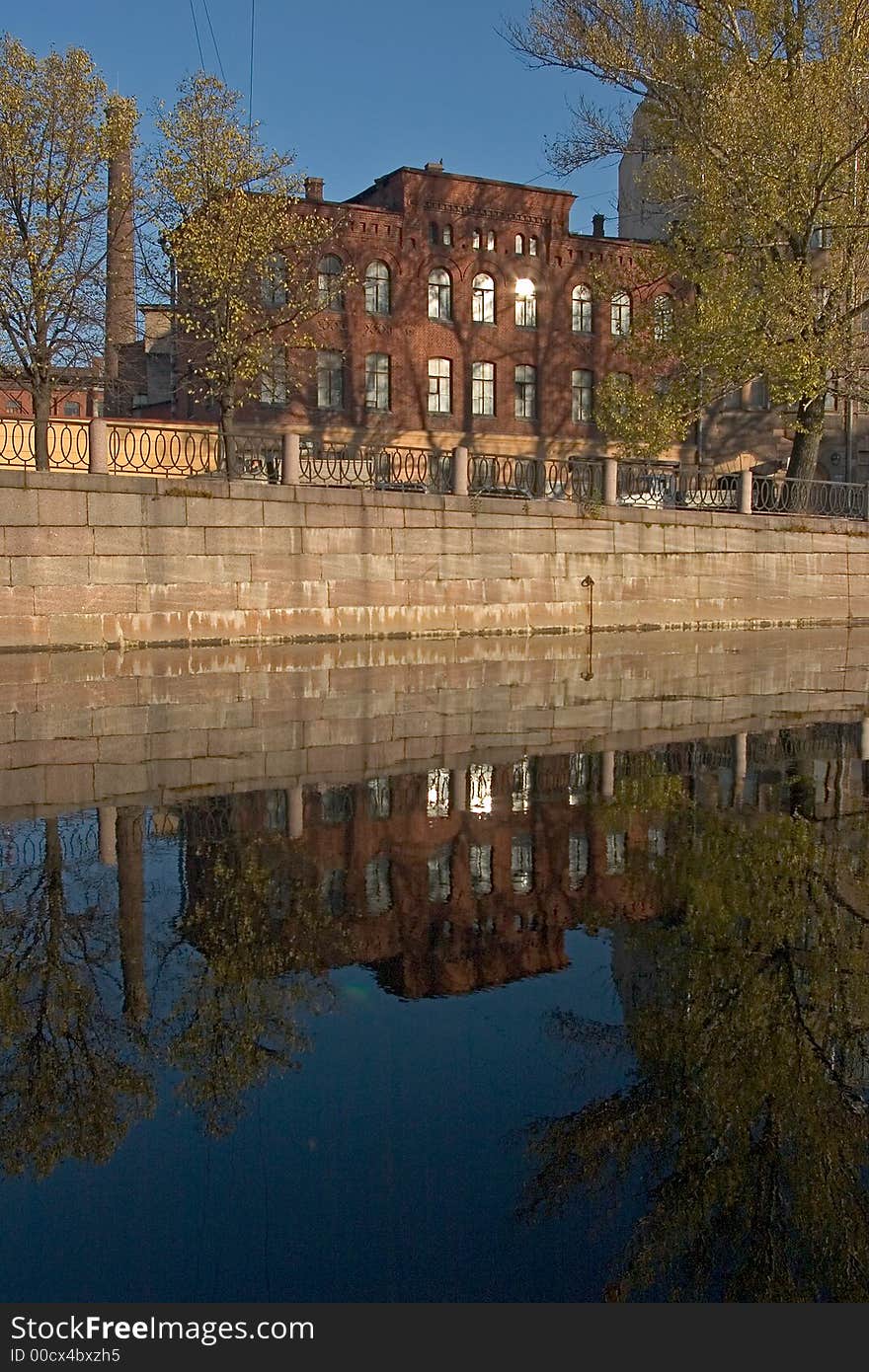 Reflection vinous building, reflection yellow- green trees, blue sky, grey quay