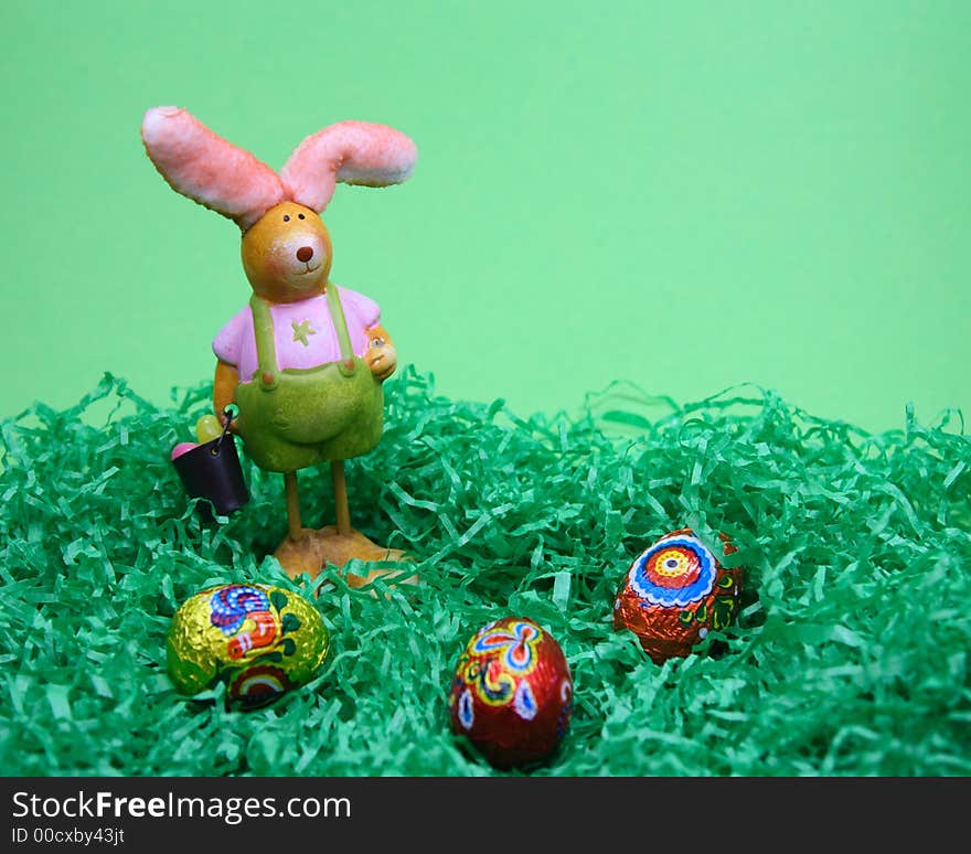 Rabbit and sweet eggs in grass on green background