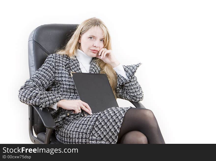 A woman wearing a suit and holding a folder sitting in a black chair. A woman wearing a suit and holding a folder sitting in a black chair