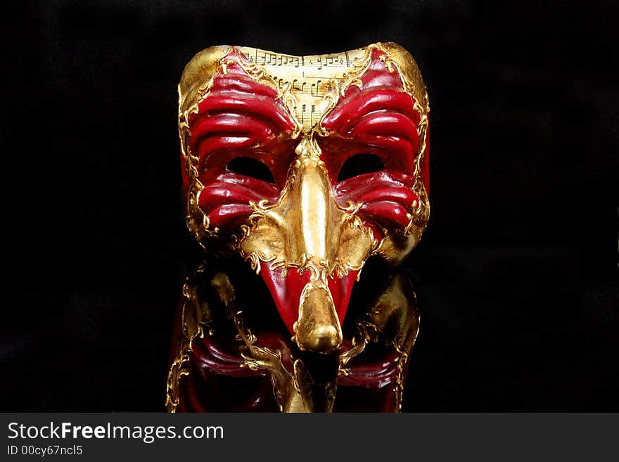 Traditional Venetian Mask in red and gold against reflective black background