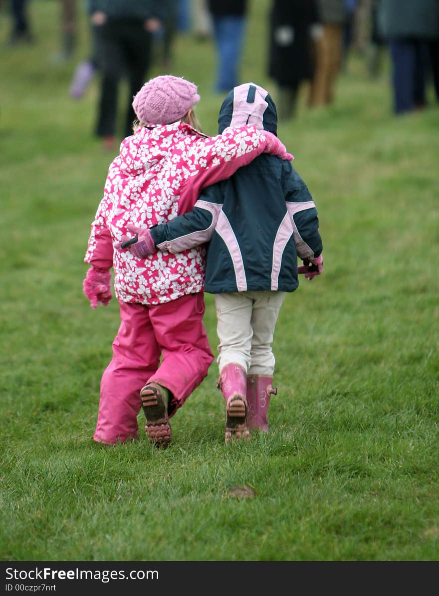 Two little girls dressed for cold weather walk away with their arms around each other. Two little girls dressed for cold weather walk away with their arms around each other