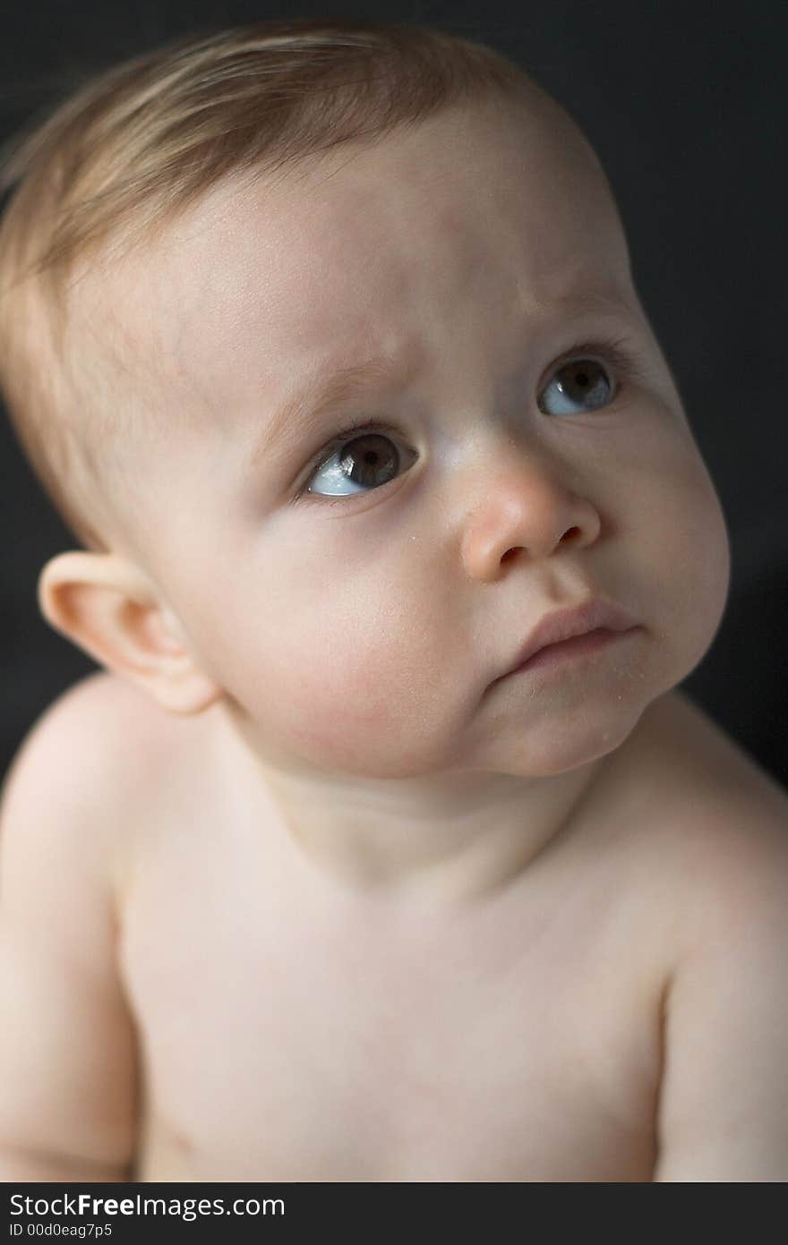 Image of a beautiful 10 month old baby boy sitting in front of a black background. Image of a beautiful 10 month old baby boy sitting in front of a black background