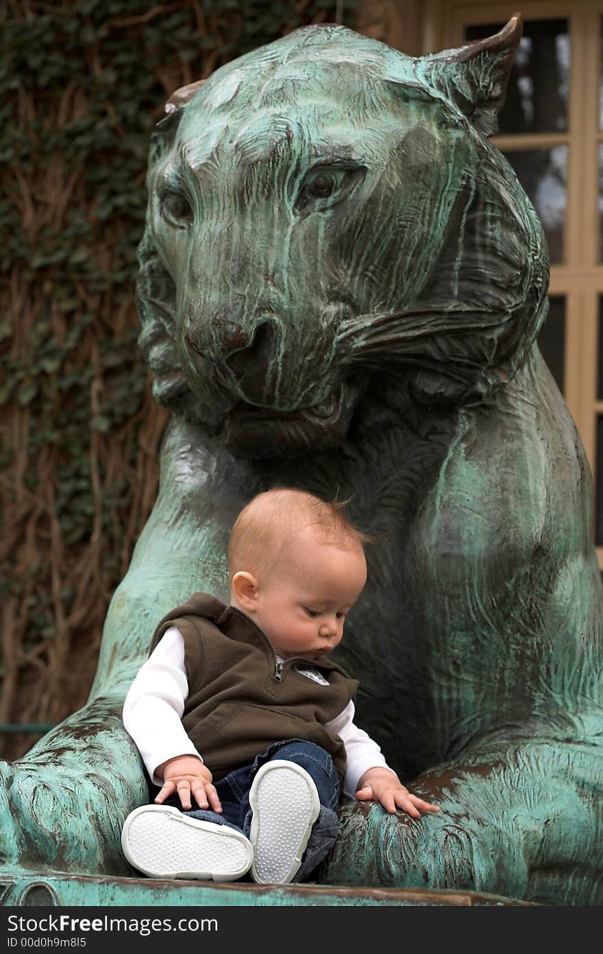 Image of cute baby sitting in front of a lion sculpture. Image of cute baby sitting in front of a lion sculpture