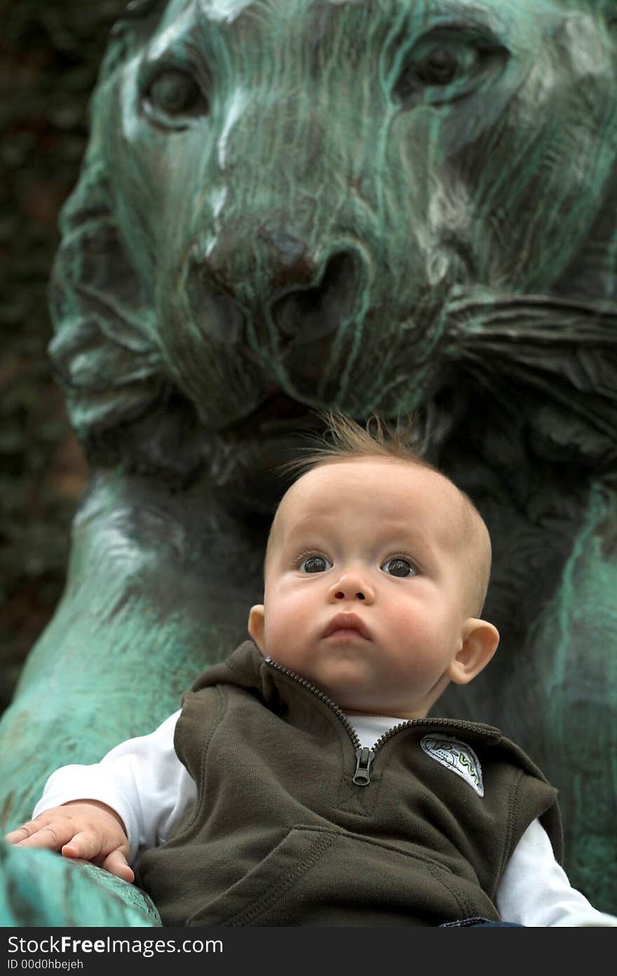 Image of cute baby sitting in front of a lion sculpture. Image of cute baby sitting in front of a lion sculpture