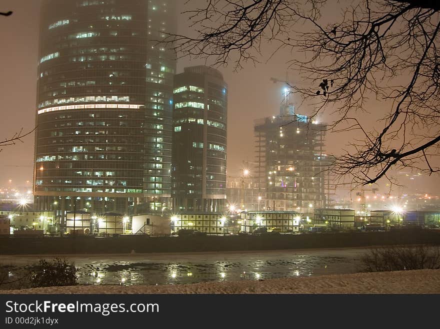 Highrise buildings, river and fog at night city.