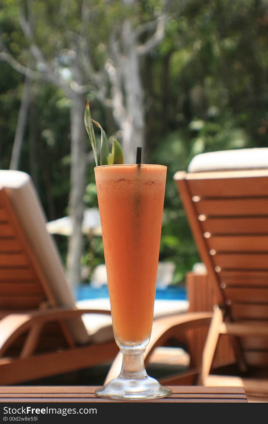 Fruit juice at a resort with deck chairs and pool in back ground