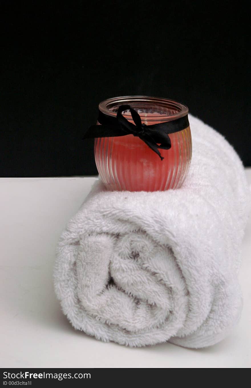 Pretty pink boudoir style candle with ribbon and clean crisp white towel for a romantic bath or spa treatment. Pretty pink boudoir style candle with ribbon and clean crisp white towel for a romantic bath or spa treatment