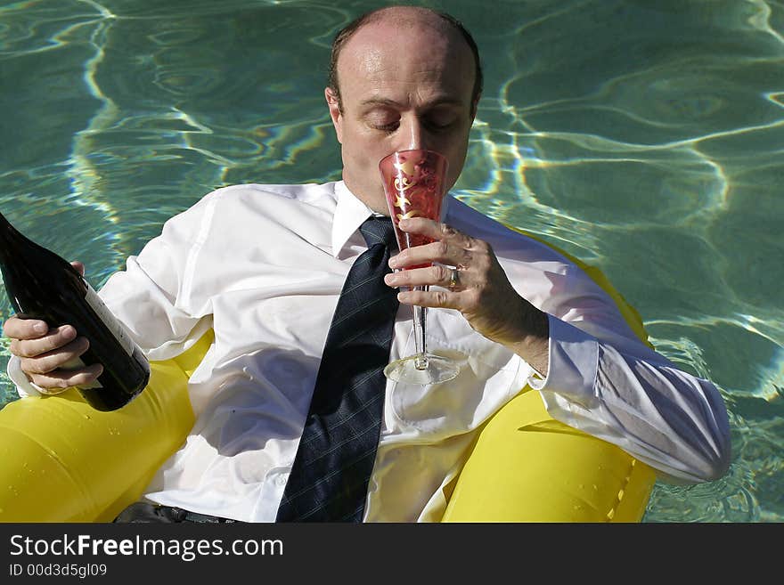 Businessman in business attire in the ocean on an inflatable boat, sipping wine in one hand whilst holding the bottle in the other, also showing the crystal clear ocean around him. Businessman in business attire in the ocean on an inflatable boat, sipping wine in one hand whilst holding the bottle in the other, also showing the crystal clear ocean around him.