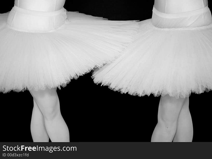 Two Ballerinas standing in a drak black room with a white tutu