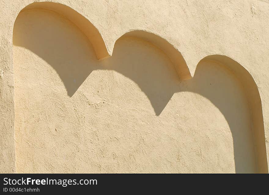 A stucco wall with three arches casting shadows